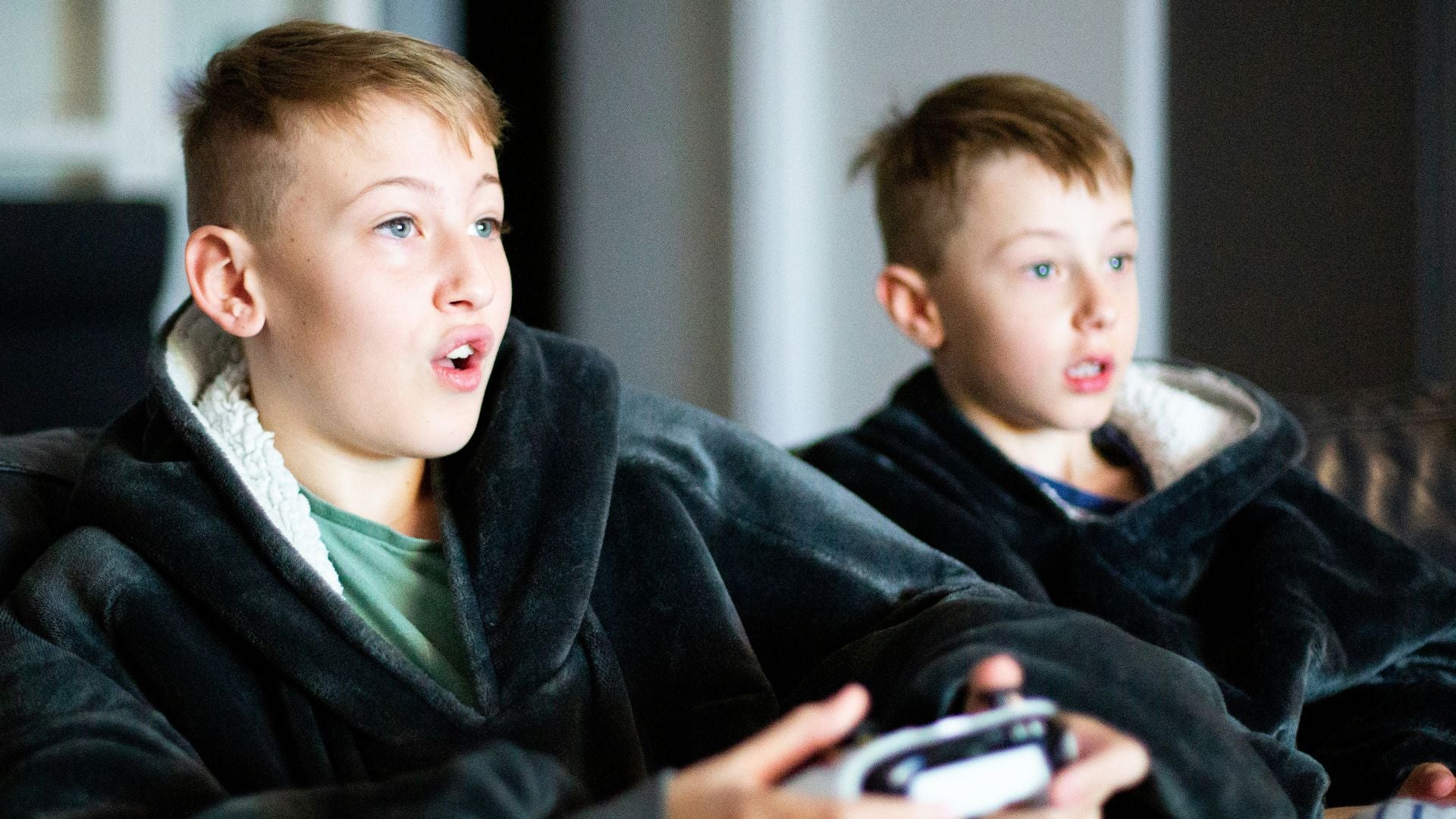 Two boys, brothers, playing video games on the TV, showing surprise 