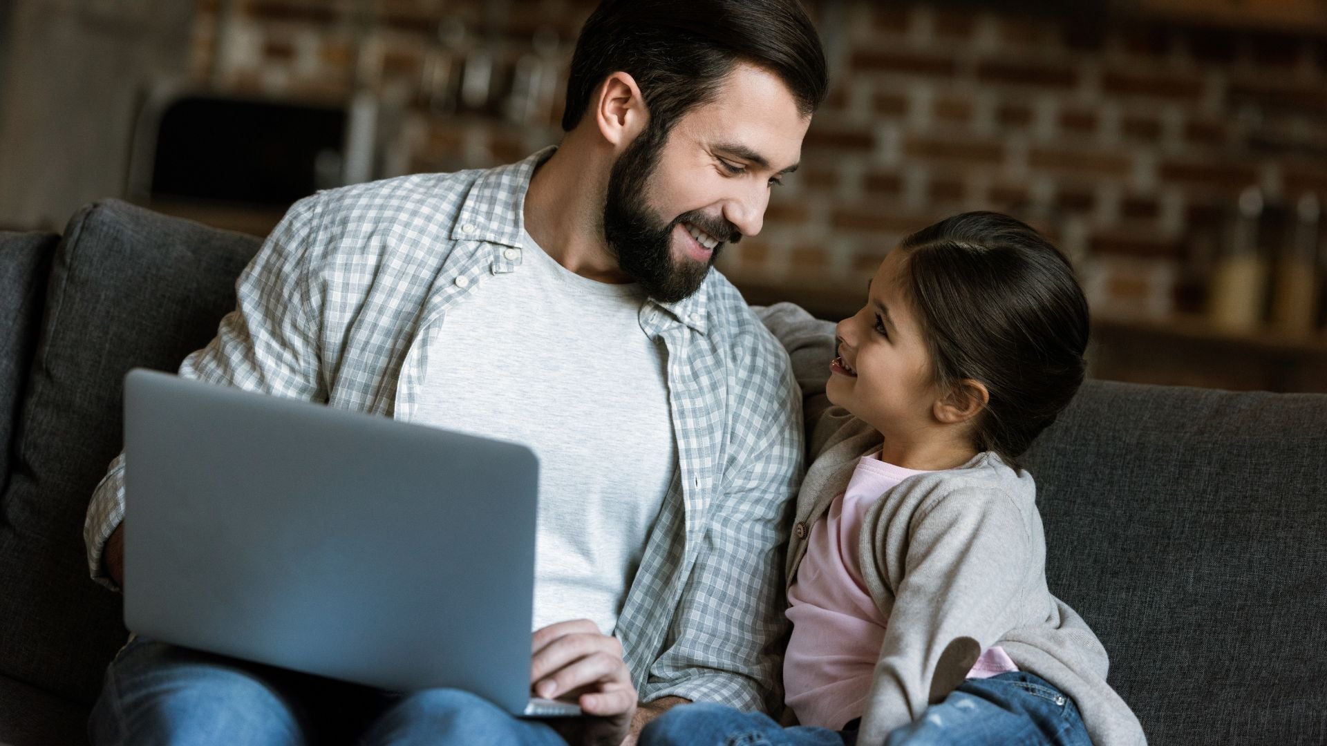 Dad and girl smiling at each other on the sofa while discussing digital topics