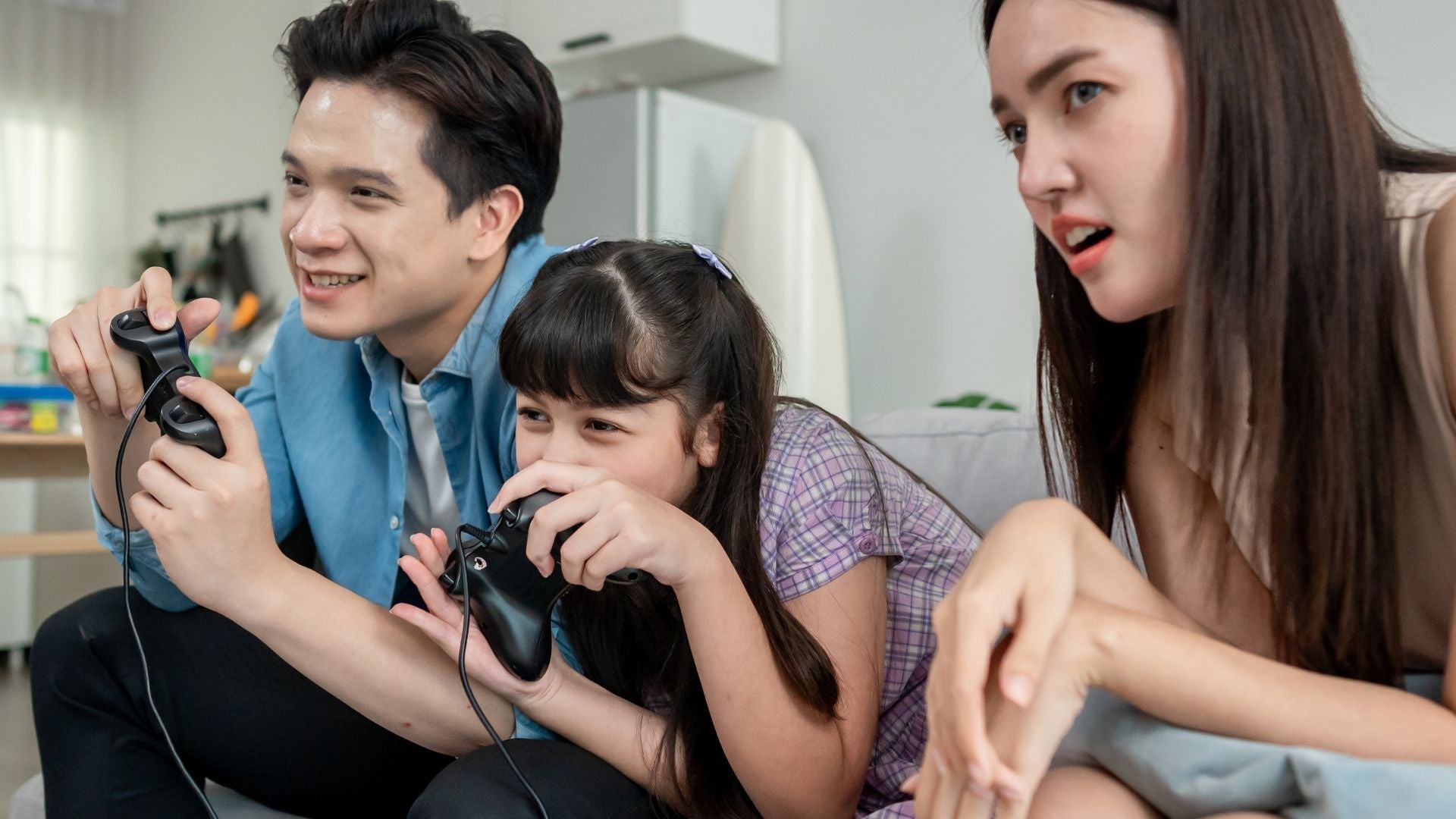 Parents playing  video games with their daughter, laughing and smiling together  